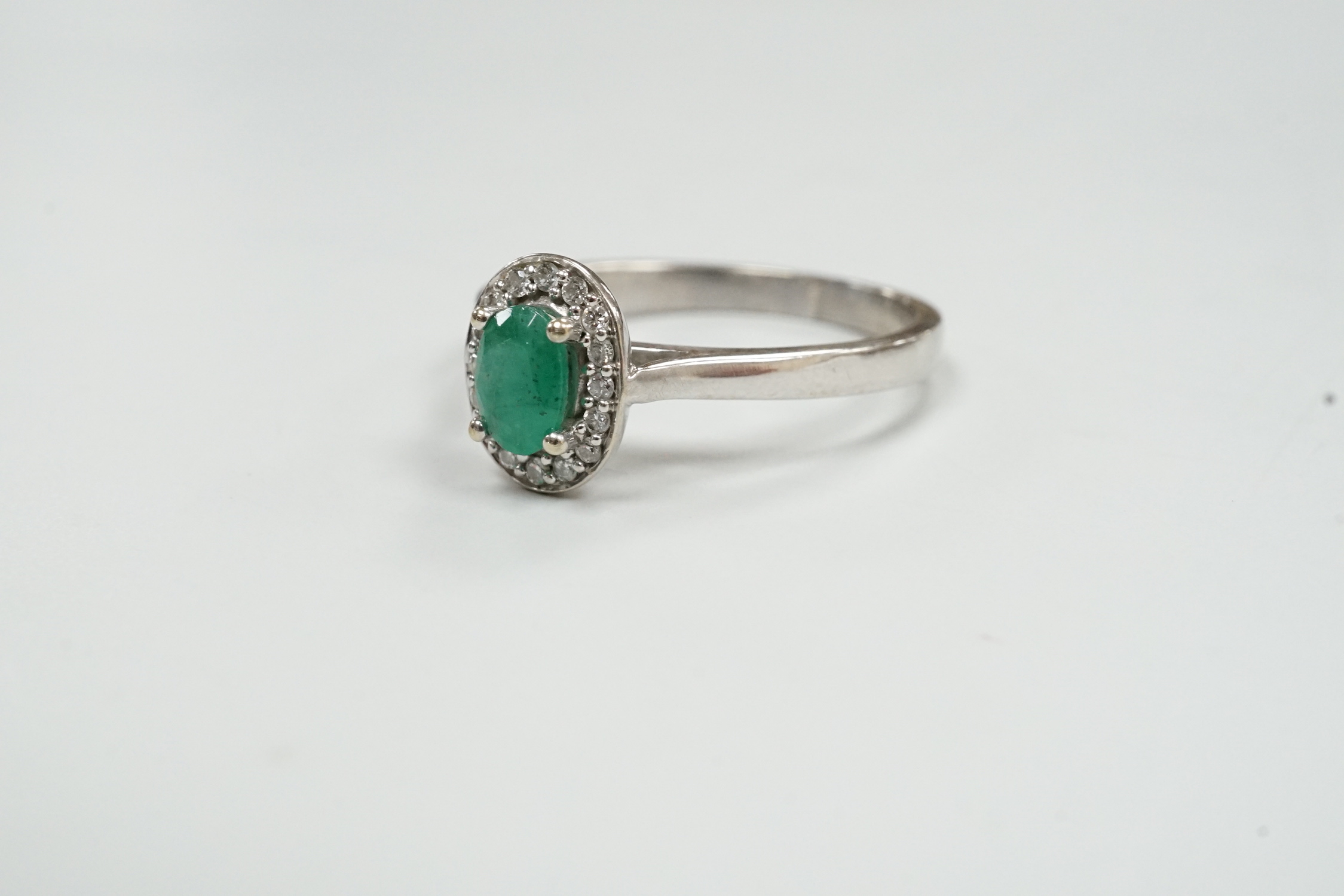 A modern 18ct white gold, emerald and diamond set oval cluster ring, size S, gross weight 3 grams.